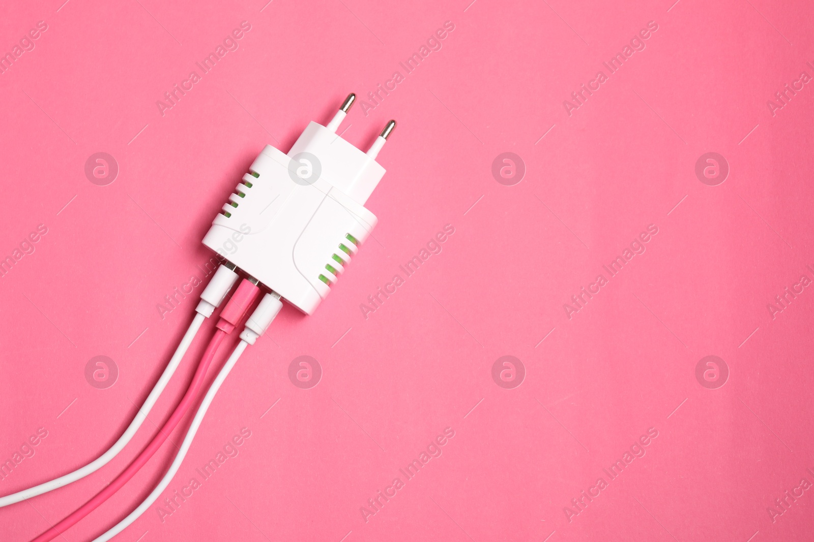 Photo of USB power adapter with charge cables on pink background, top view. Space for text