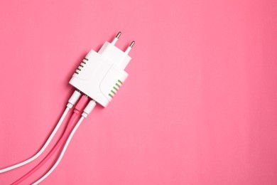 Photo of USB power adapter with charge cables on pink background, top view. Space for text