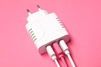 Photo of USB power adapter with charge cables on pink background, closeup