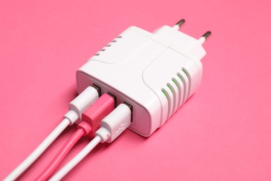 Photo of USB power adapter with charge cables on pink background, closeup