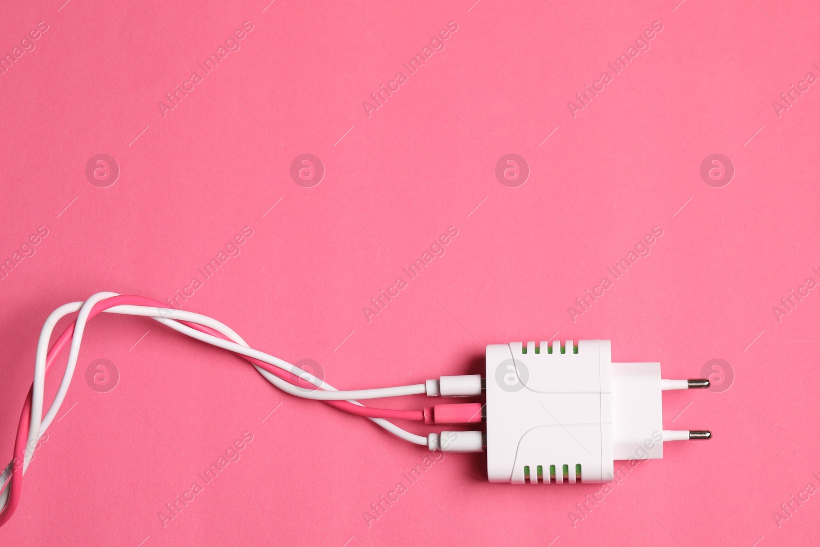 Photo of USB power adapter with charge cables on pink background, top view. Space for text