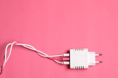 Photo of USB power adapter with charge cables on pink background, top view. Space for text