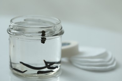 Photo of Medicinal leeches in glass jar and cotton pads on white table, closeup. Space for text