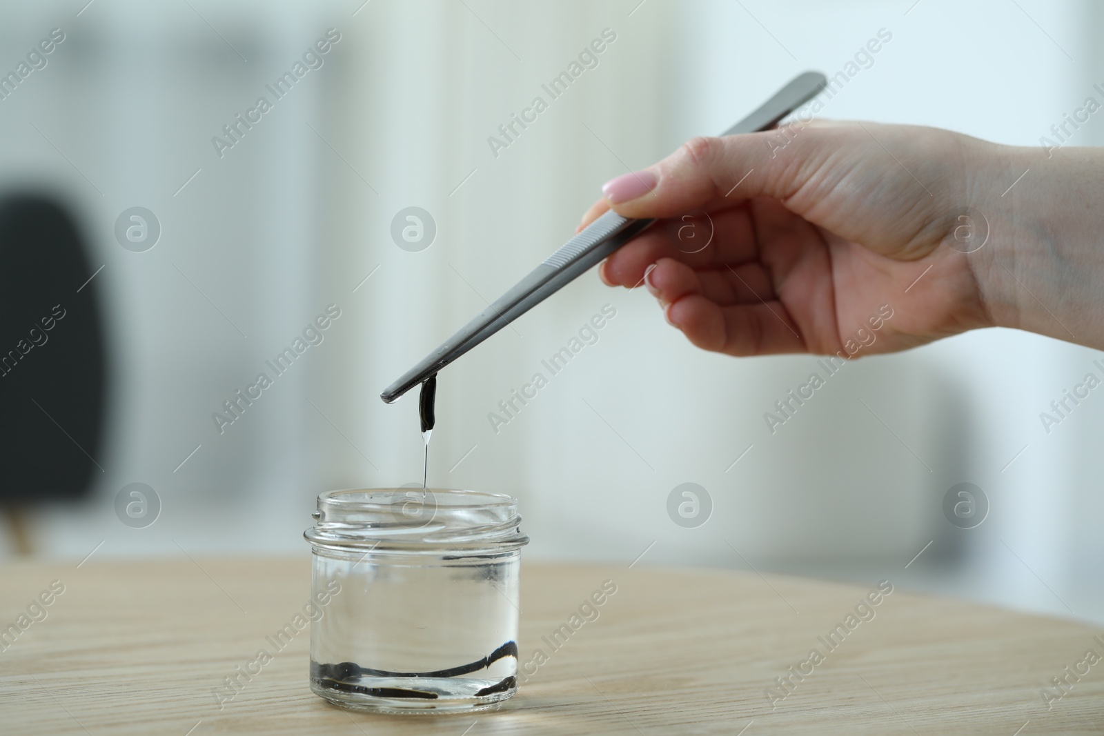 Photo of Woman taking leech from jar with tweezers on wooden table, closeup