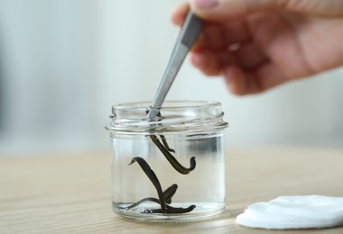 Photo of Woman taking leech from jar with tweezers on wooden table, closeup