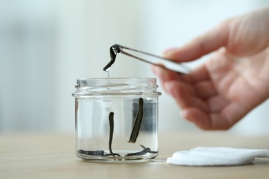 Photo of Woman taking leech from jar with tweezers on wooden table, closeup