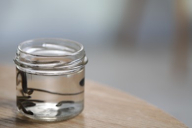 Photo of Medicinal leeches in glass jar on wooden table, closeup. Space for text