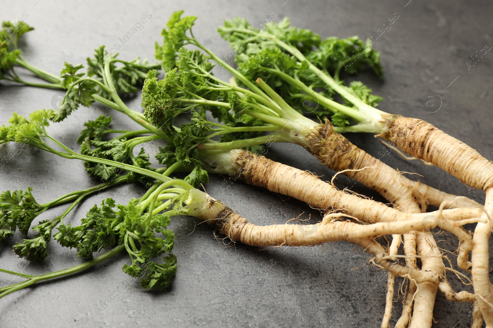 Photo of Parsley roots with leaves on black table, closeup