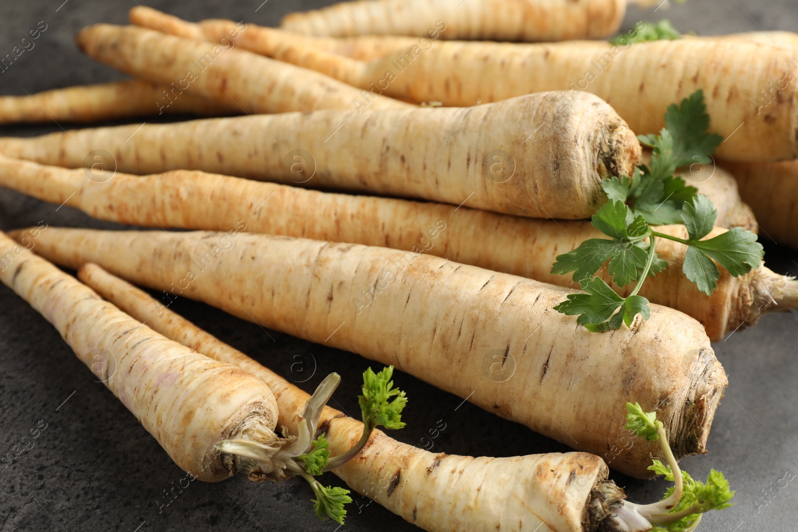 Photo of Parsley roots with leaves on black table, closeup