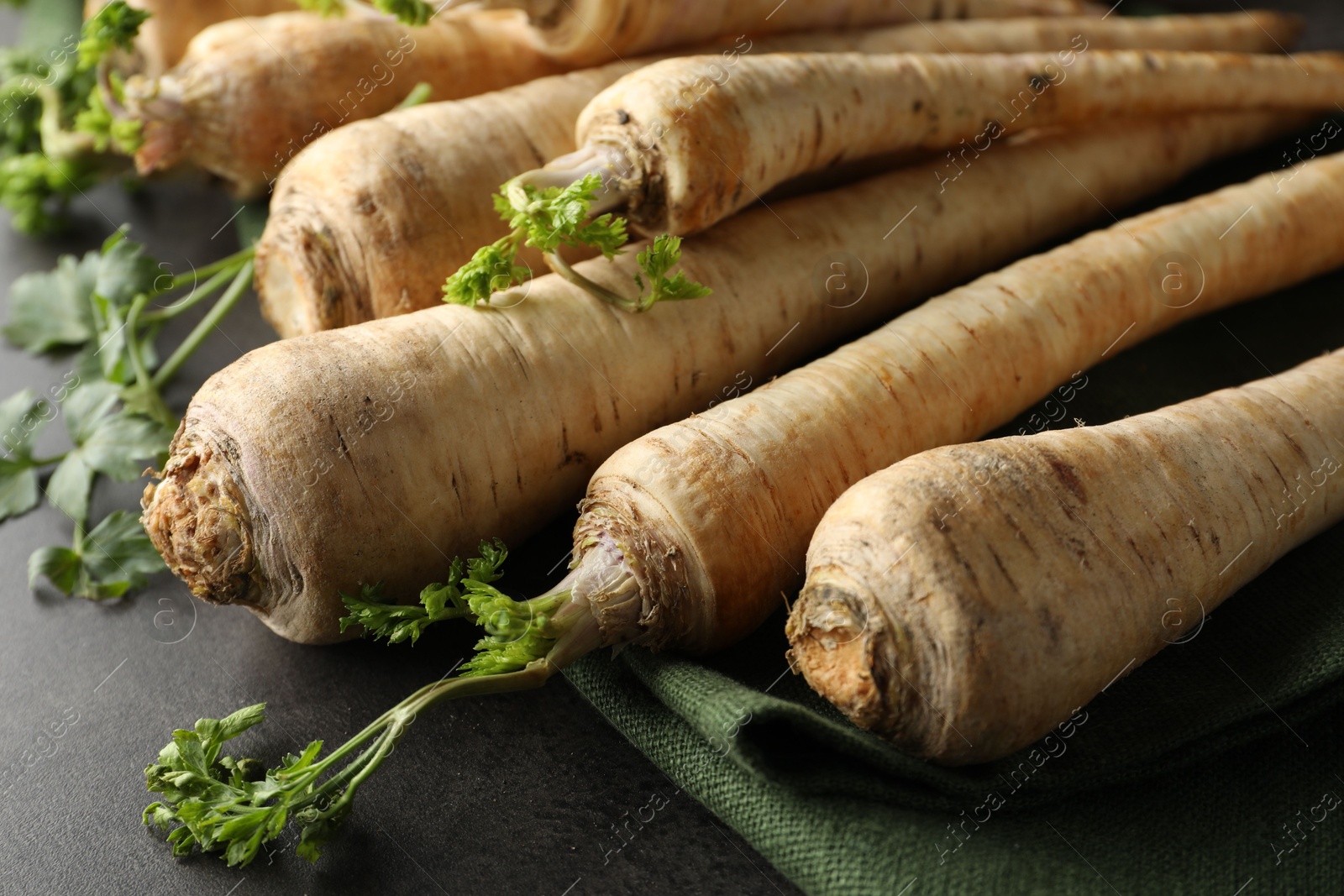 Photo of Parsley roots with leaves on black table, closeup