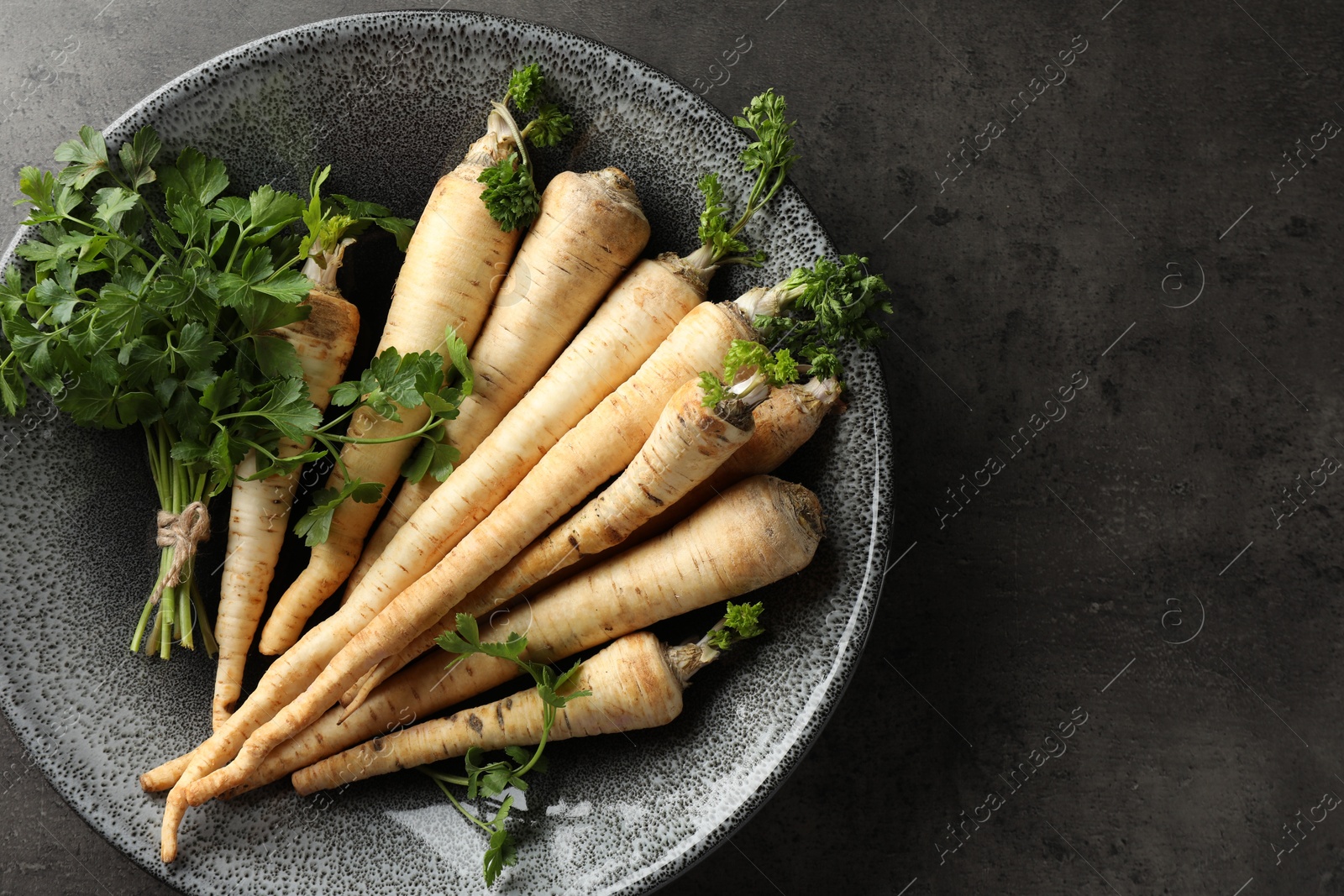 Photo of Parsley roots with leaves on black table, top view. Space for text