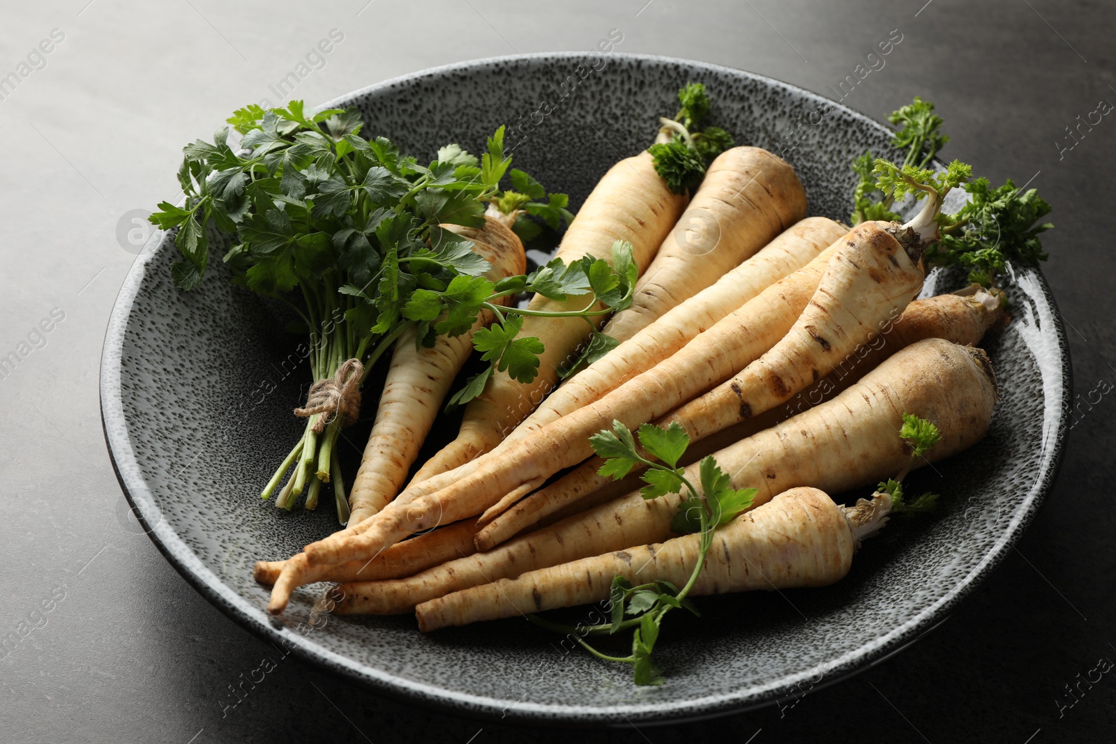 Photo of Parsley roots with leaves on black table, closeup