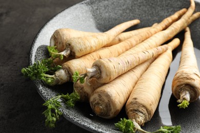 Photo of Parsley roots with leaves on black table, closeup