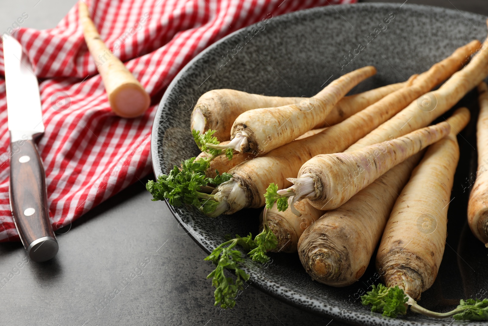 Photo of Parsley roots with leaves and knife on black table, closeup