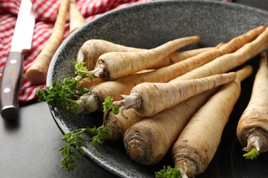 Photo of Parsley roots with leaves and knife on black table, closeup