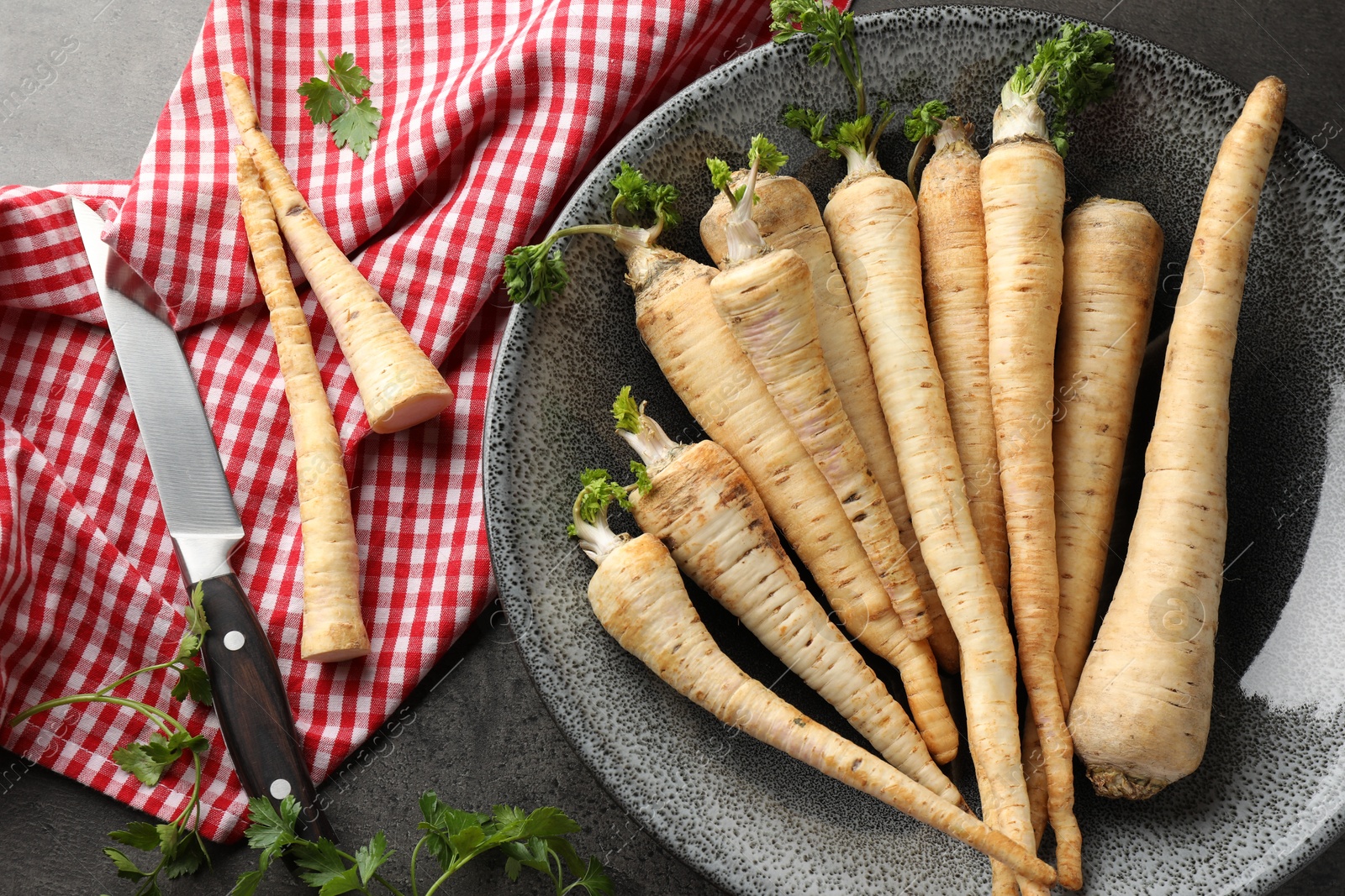 Photo of Parsley roots with leaves and knife on black table, flat lay