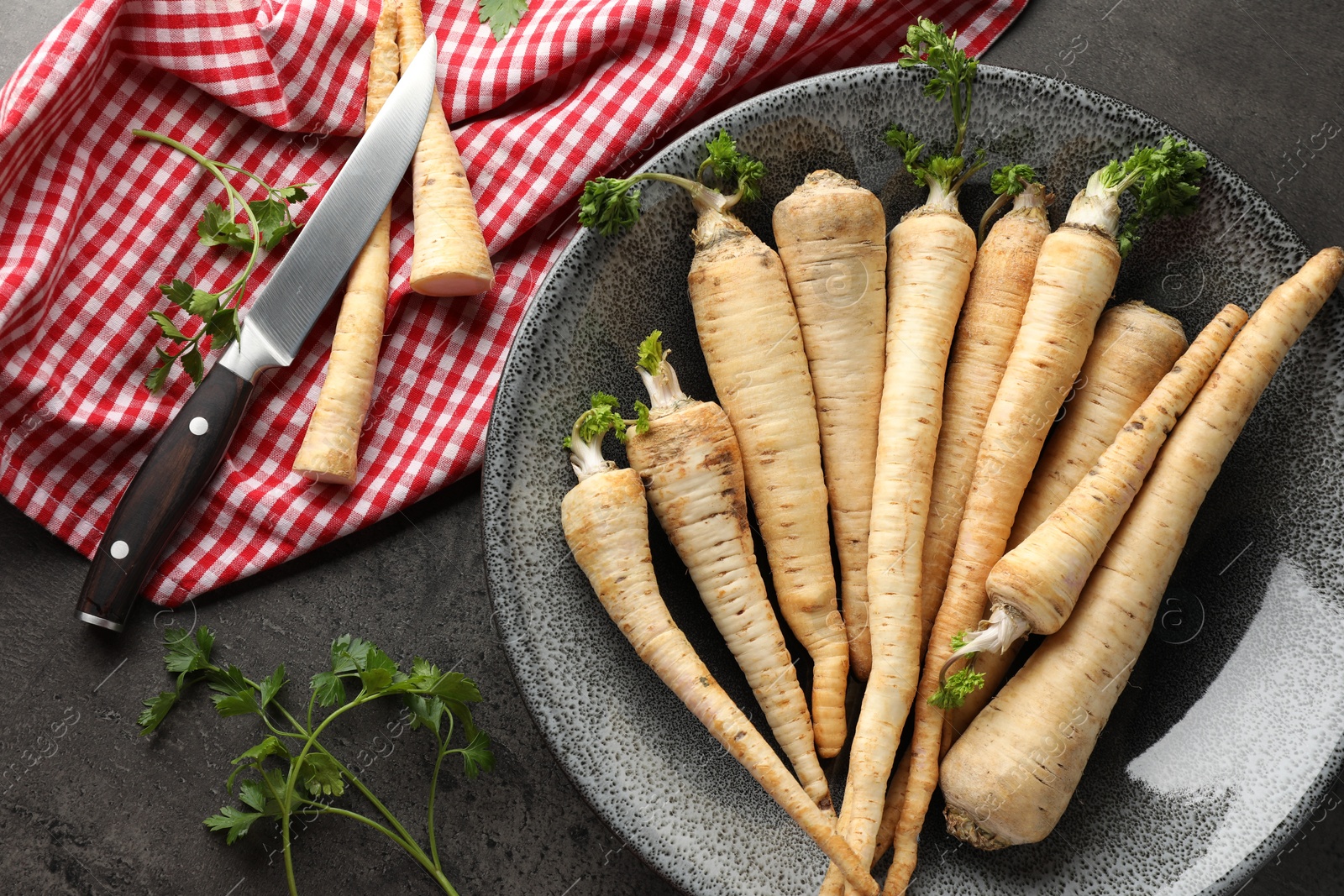 Photo of Parsley roots with leaves and knife on black table, flat lay