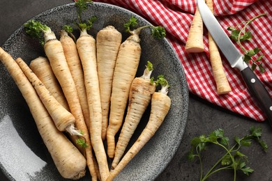 Photo of Parsley roots with leaves and knife on black table, flat lay