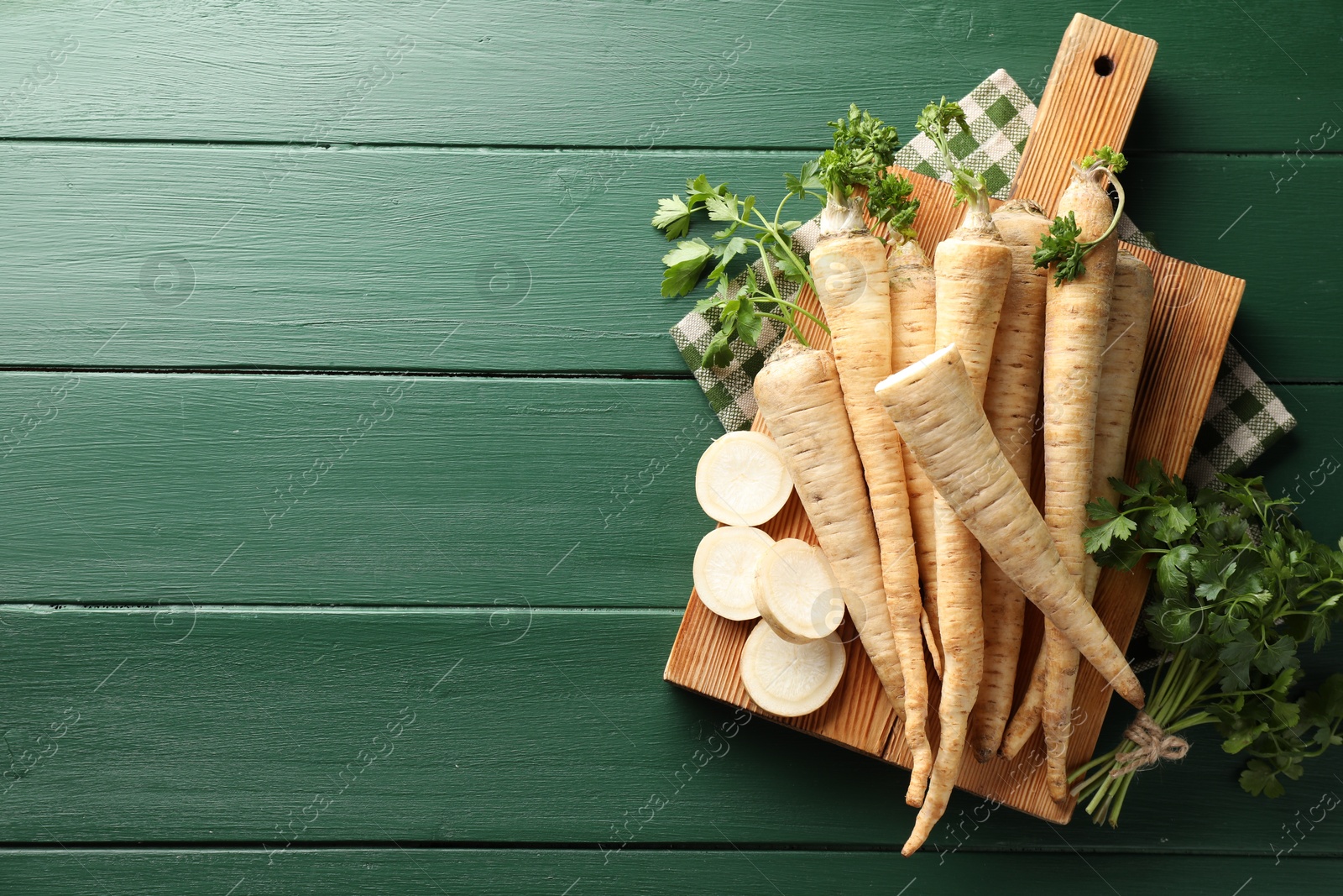 Photo of Parsley roots and leaves on green wooden table, top view. Space for text