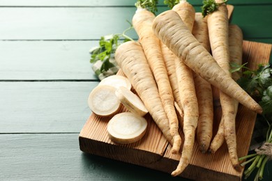 Photo of Parsley roots and leaves on green wooden table, closeup. Space for text