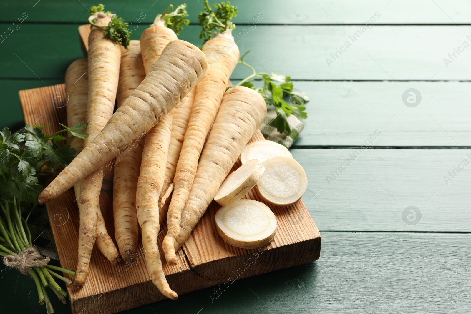 Photo of Parsley roots and leaves on green wooden table, closeup. Space for text