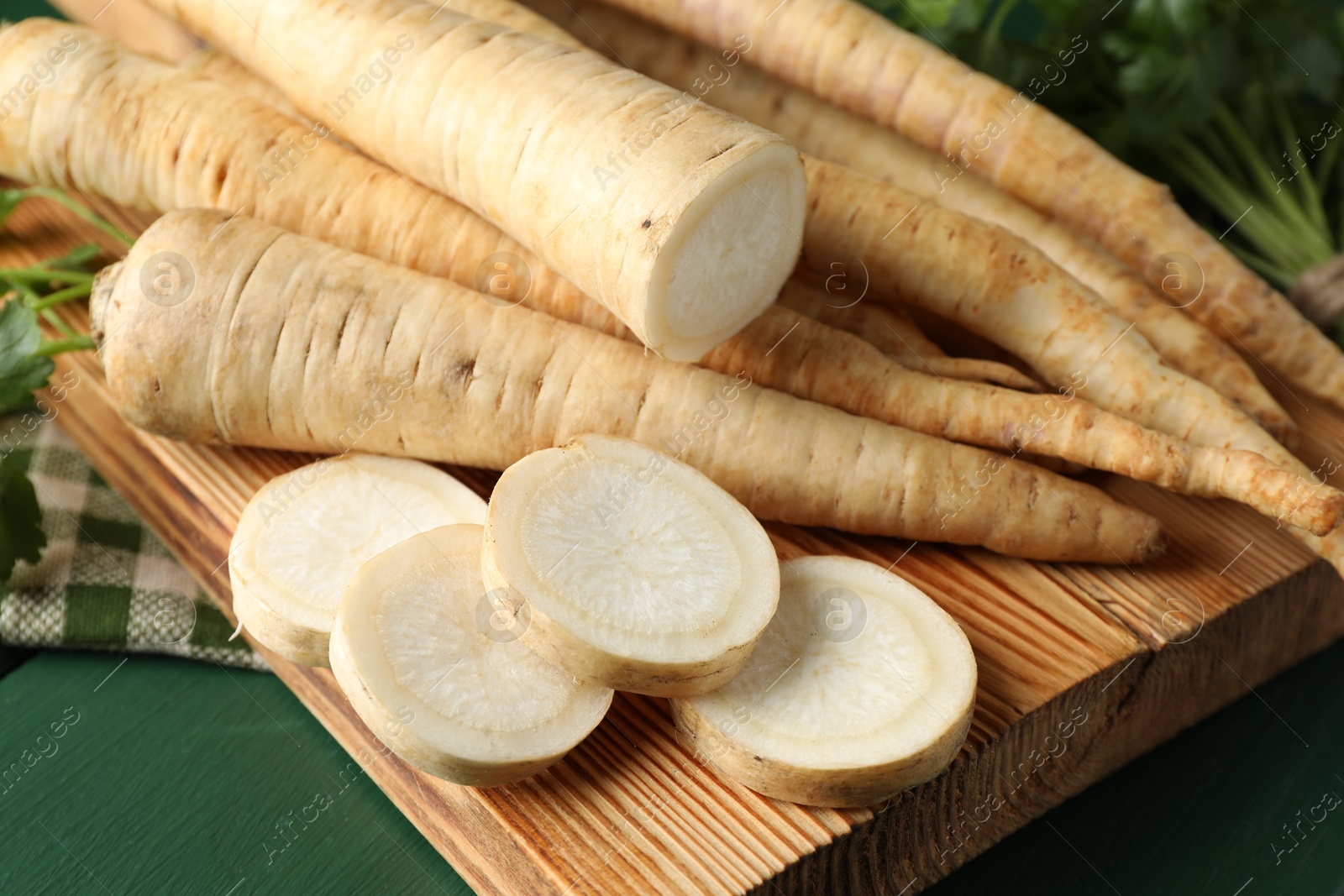 Photo of Whole and cut parsley roots on green wooden table, closeup