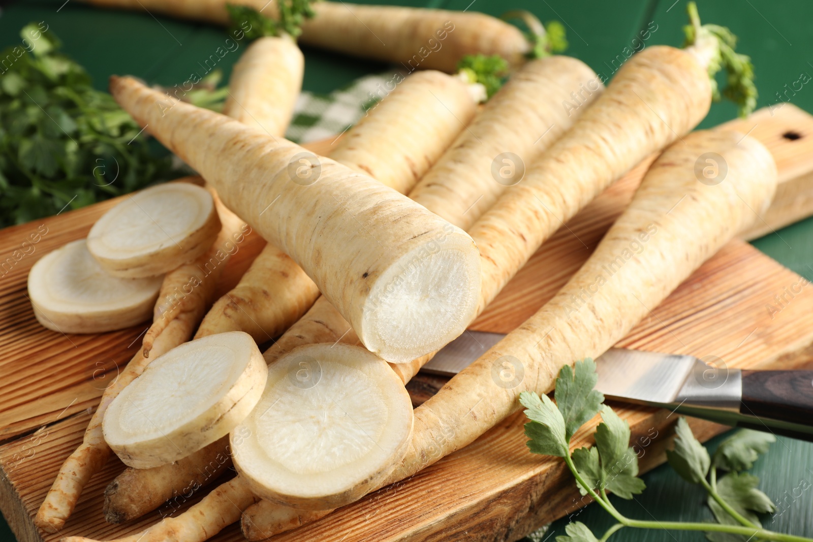 Photo of Parsley roots and leaves with knife on green wooden table, closeup