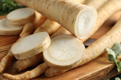 Photo of Whole and cut parsley roots on wooden table, closeup