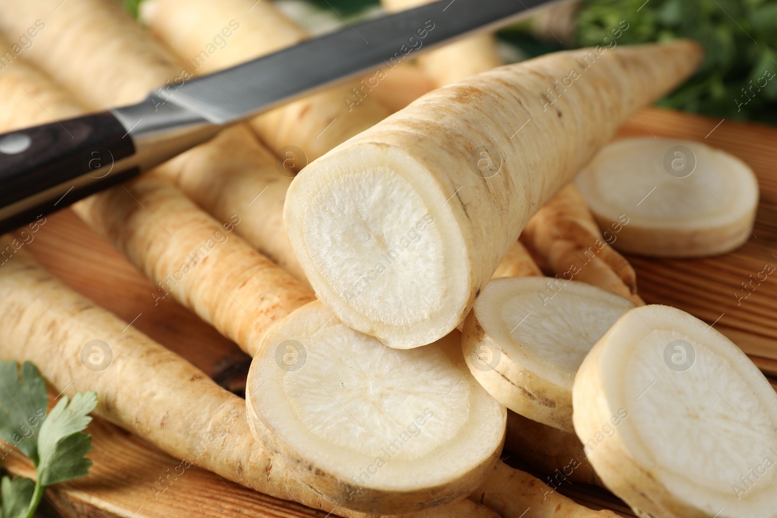 Photo of Whole and cut parsley roots with knife on wooden table, closeup