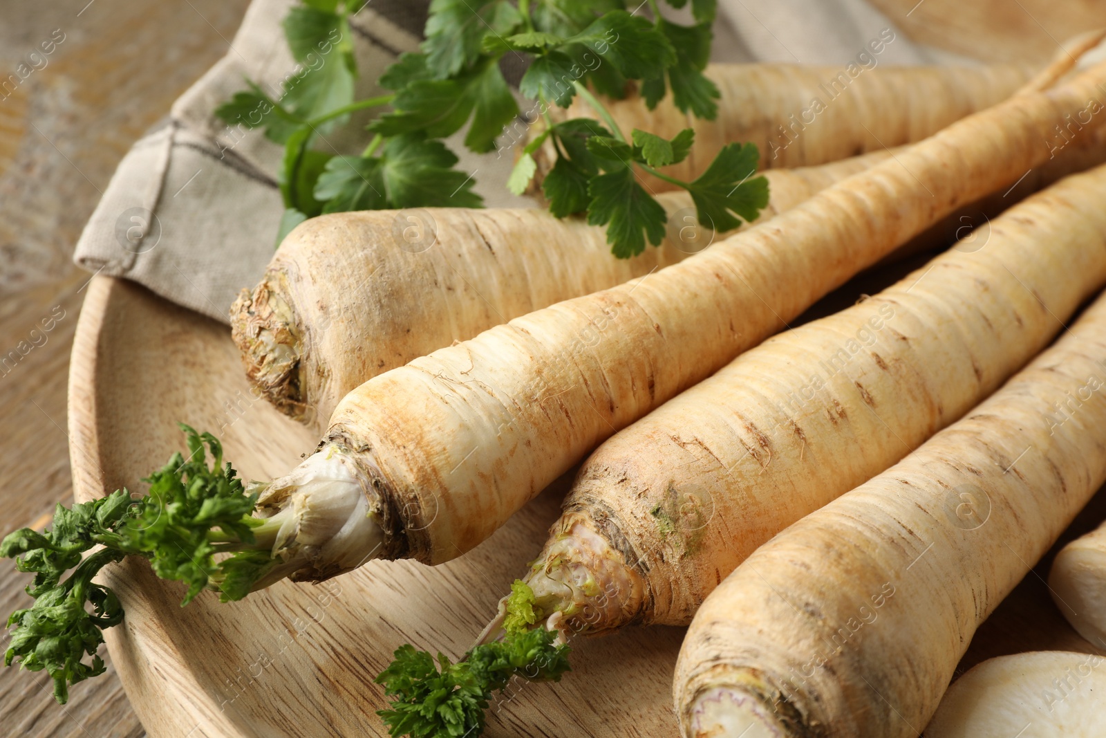 Photo of Raw parsley roots with leaves on wooden table, closeup