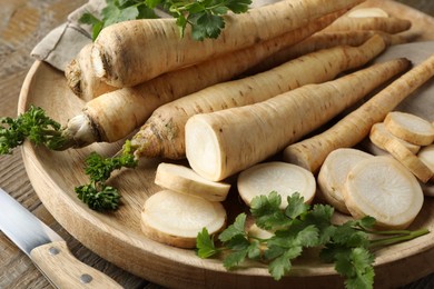 Photo of Parsley roots and leaves with knife on wooden table, closeup