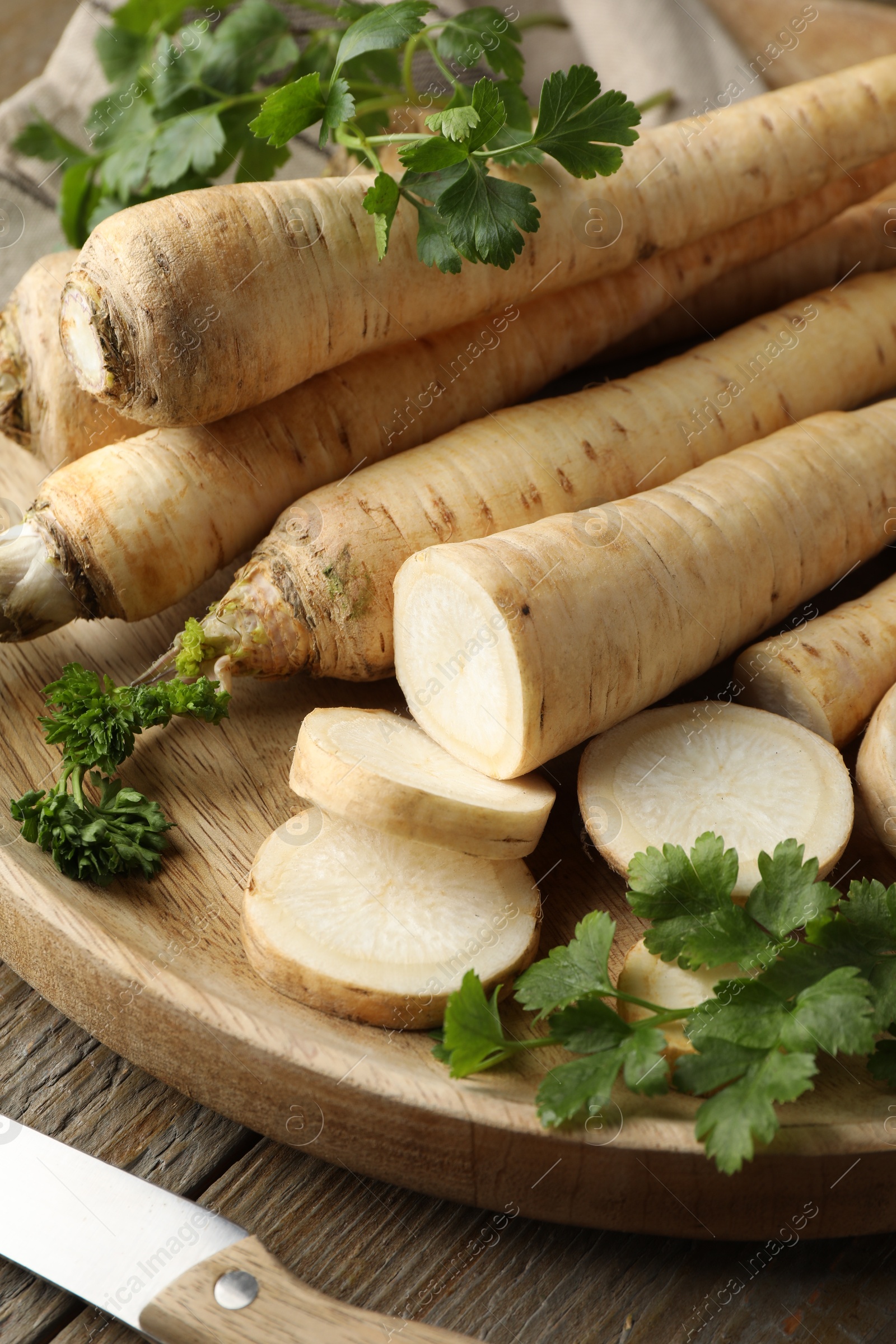 Photo of Parsley roots and leaves with knife on wooden table, closeup