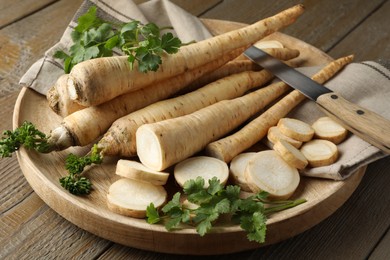 Photo of Parsley roots and leaves with knife on wooden table, closeup