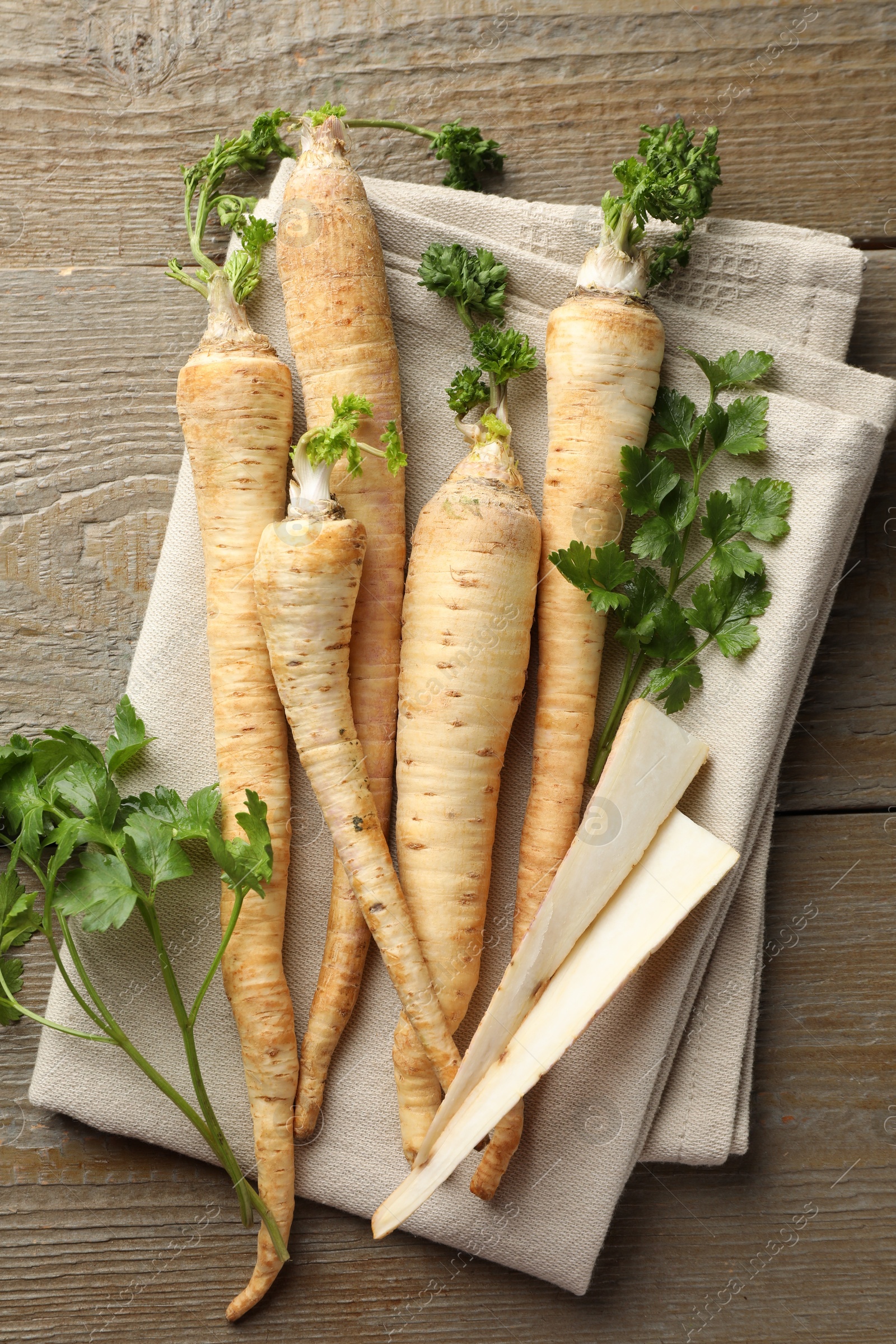 Photo of Raw parsley roots with leaves on wooden table, top view