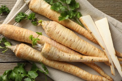 Photo of Raw parsley roots with leaves on wooden table, flat lay