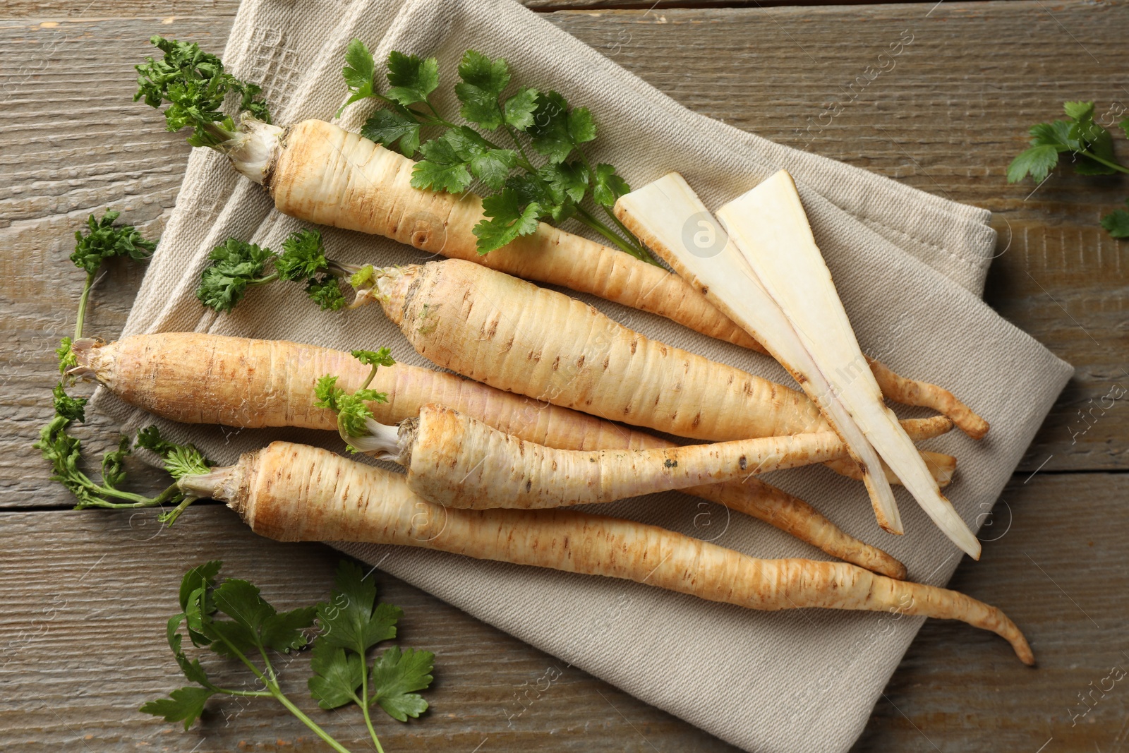 Photo of Raw parsley roots with leaves on wooden table, flat lay