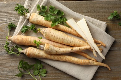 Photo of Raw parsley roots with leaves on wooden table, flat lay