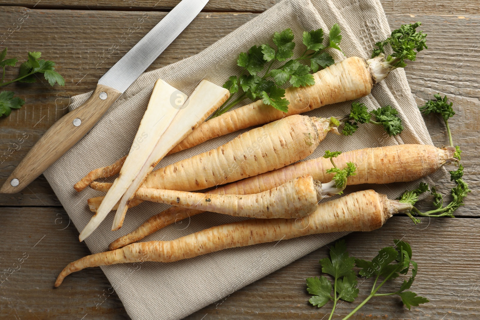 Photo of Raw parsley roots with leaves and knife on wooden table, flat lay