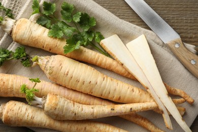 Photo of Raw parsley roots with leaves and knife on wooden table, flat lay