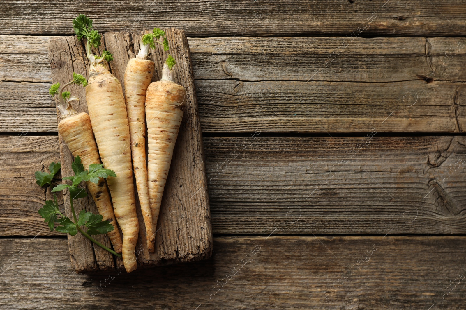 Photo of Raw parsley roots with leaves on wooden table, top view. Space for text