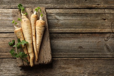 Photo of Raw parsley roots with leaves on wooden table, top view. Space for text