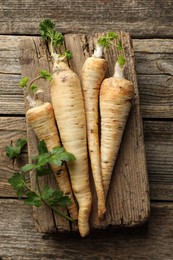 Photo of Raw parsley roots with leaves on wooden table, top view