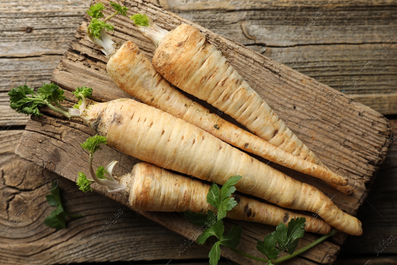 Photo of Raw parsley roots with leaves on wooden table, top view