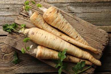 Photo of Raw parsley roots with leaves on wooden table, top view