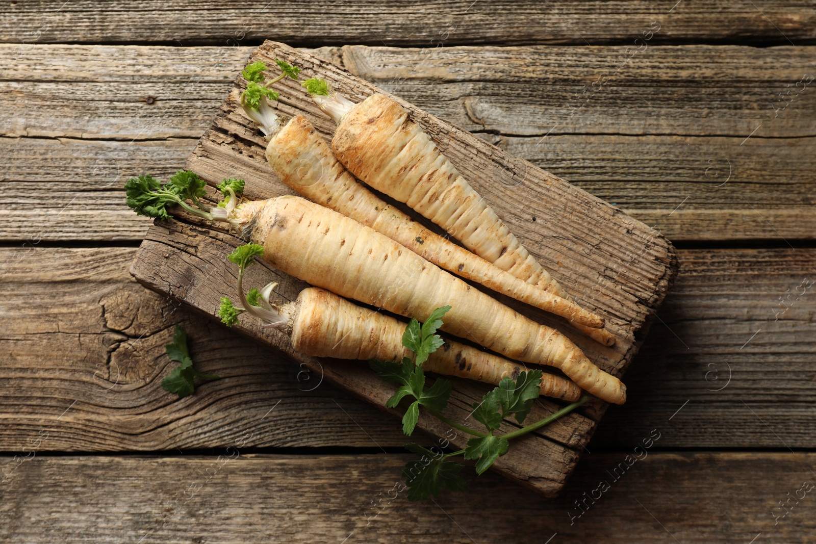 Photo of Raw parsley roots with leaves on wooden table, top view