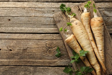 Photo of Raw parsley roots with leaves on wooden table, top view. Space for text