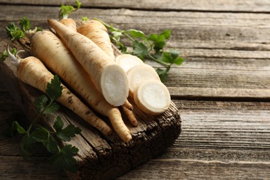 Photo of Parsley roots and leaves on wooden table, closeup. Space for text