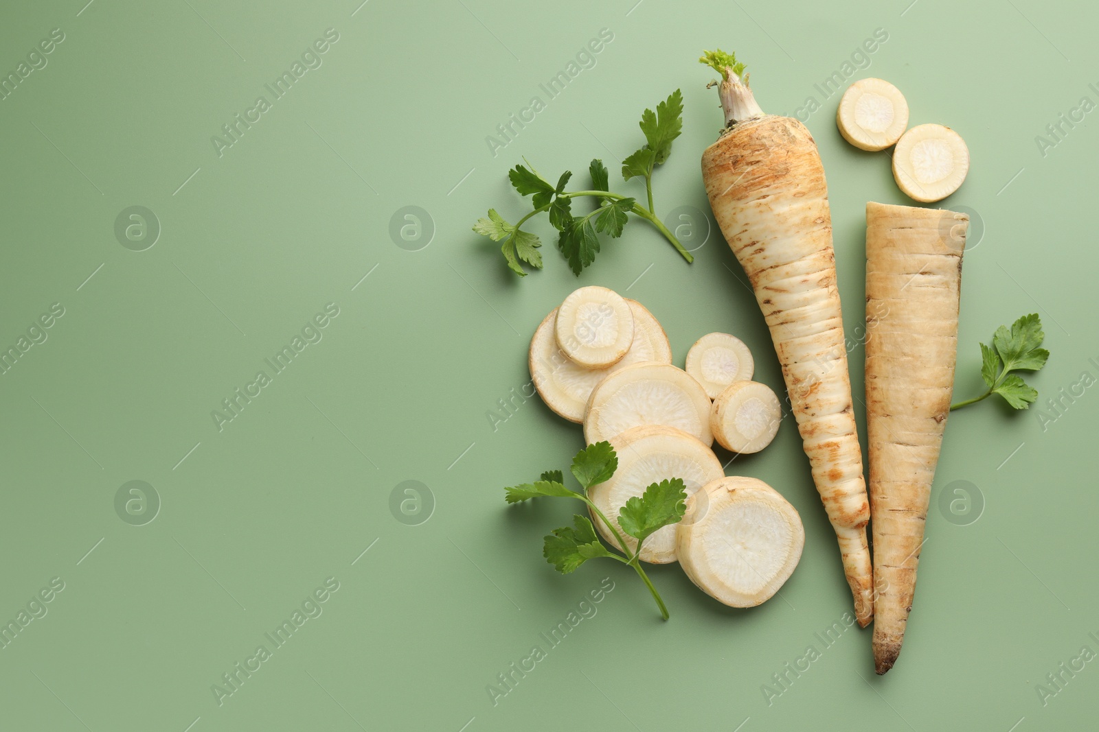 Photo of Parsley roots and leaves on green background, flat lay. Space for text