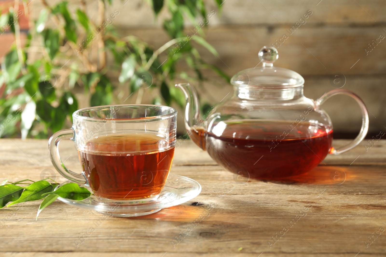 Freshly brewed tea in glass cup and teapot on wooden table Photo of Freshly brewed tea in glass cup and teapot on wooden table