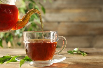 Pouring freshly brewed tea from teapot into glass cup on wooden table, closeup